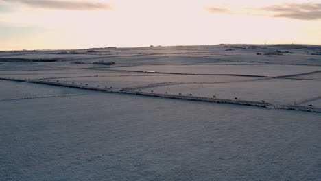 Panoramic-aerial-overview-of-sunset-sky-spreading-soft-light-on-snow-covered-farm-fields