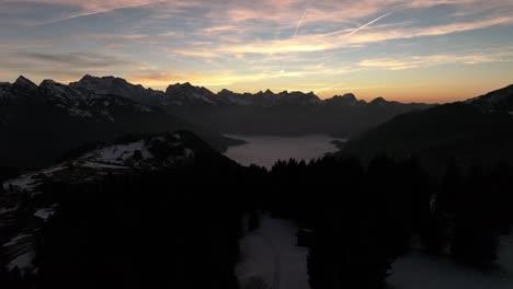 Drohne-Fliegt-über-Berge,-Im-Tal-Sind-Nebelwolken-Und-In-Der-Ferne-Hohe-Berge-Mit-Schnee-In-Amden,-Weesen,-Glarus,-Schweiz,-Sonnenaufgangsstimmung