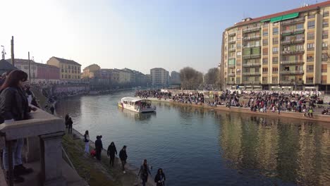 Massen-Von-Touristen-Umgeben-Den-Kanal,-Während-Ein-Boot-Voller-Menschen-Den-Kanal-In-Der-Via-Vigevano,-Mailand,-Italien-Entlang-Fährt.