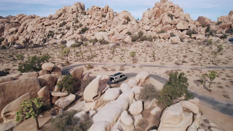 Ein-Mercedes-Sprinter-Van-Parkt-Im-Joshua-Tree-Nationalpark,-Während-Eine-Drohne-Rückwärts-Fliegt