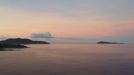 Infinite-view-of-pink-and-blue-skies-during-sunset-over-a-smooth,-reflective-ocean-surface,-with-tropical-islands-in-the-distance