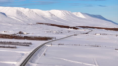 Aerial-trucking-view-of-traffic-driving-over-road-between-snow-covered-mountains-in-Iceland