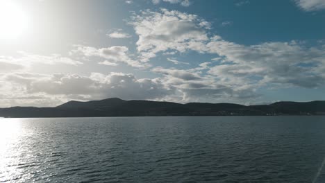 A-rotating-silhouette-drone-shot-a-village-mountain,-warm-weather,-flying-above-a-dreamy-lake,-4K-video,-European-spring-nature,-beautiful-landscape,-white-scenic-clouds