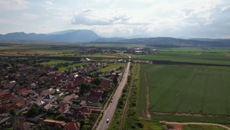 Ciudad-De-Rasnov-Con-Exuberantes-Campos,-Colinas-Y-Casas-A-La-Luz-Del-Día,-Vista-Aérea