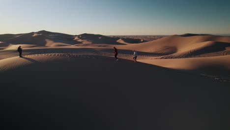 four-men-people-walking-in-the-desert-on-the-dunes-at-sunrise,-golden-hour