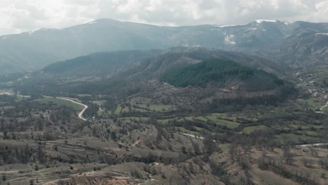 A-drone-shot-of-forest-mountains-with-snow,-warm-weather,-little-village,-flying-forward-a-dreamy-hill,-4K-video,-European-winter-nature,-scenic-white-clouds,-beautiful-landscape