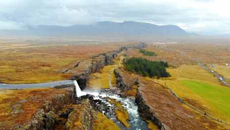 An-Aerial,-4K-Drone-shots-of-a-cascading-waterfall-in-the-middle-of-the-colorful-Iceland,-scenic,-terrain,-tranquil-landscape