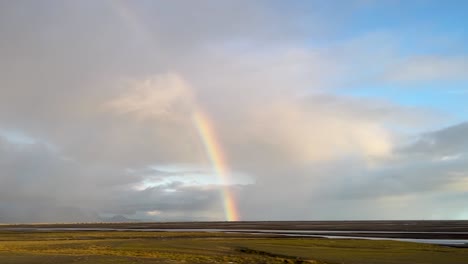 Vibrant-rainbow-arching-across-Icelandic-plains-with-vast-open-skies,-POV-from-car