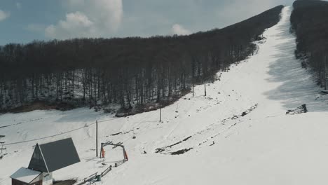 A-drone-shot-of-forest-mountain-with-snow,-warm-weather,-flying-above-the-snowboard-hill,-4K-video,-European-winter-nature