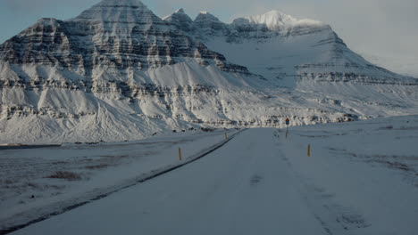 Golden-hour-glow-spread-across-snow-covered-rugged-mountain-peaks-in-iceland-at-end-of-road