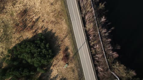 Top-down-drone-shot-of-the-autumn-lakescape-and-the-road-leading-past-the-gas-pipeline-with-passing-cars