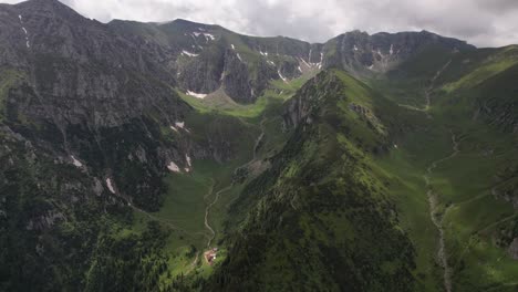 Lush-Bucegi-Mountains-with-green-slopes-under-a-cloudy-sky,-aerial-shot