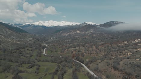 A-drone-shot-of-forest-mountains-with-snow,-warm-weather,-little-village,-flying-above-a-foggy-hill,-4K-video,-European-winter-nature,-scenic-white-clouds,-beautiful-landscape
