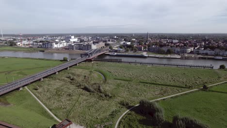 Floodplains-with-steel-draw-bridge-along-river-IJssel-with-tower-town-Zutphen,-The-Netherlands-on-the-other-wide-of-the-waterway