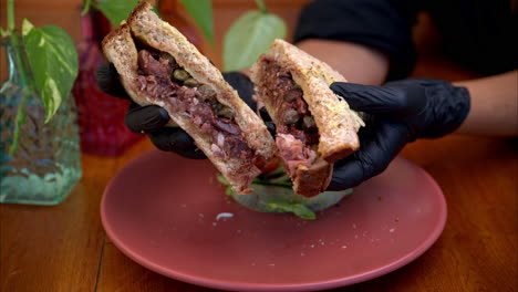 Cámara-Lenta-De-Una-Persona-Que-Usa-Guantes-De-Látex-Negros-Sosteniendo-Y-Presentando-Un-Sándwich-De-Prosciutto-Con-Salsa-De-Higos-Y-Alcaparras