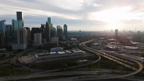 Traffic-in-front-of-the-Houston-skyline,-cloudy-sunset-in-Texas,-USA---Aerial-view