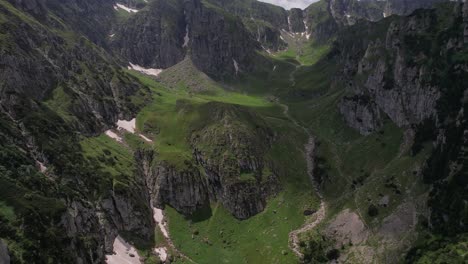Üppiges-Grünes-Tal-Inmitten-Hoch-Aufragender-Bucegi-Berge-Unter-Einem-Wolkigen-Himmel,-Luftaufnahme