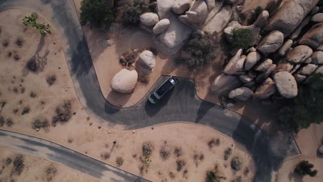 Top-down-rotating-aerials-drone-shot-of-a-Mercedes-Sprinter-van-parking-in-Joshua-Tree-National-Park-in-the-desert