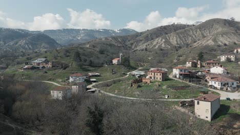 Eine-Drohnenaufnahme-Von-Waldbergen-Mit-Schnee,-Warmes-Wetter,-Kleines-Dorf,-Flug-über-Den-Verträumten-Hügel,-4K-Video,-Europäische-Winternatur