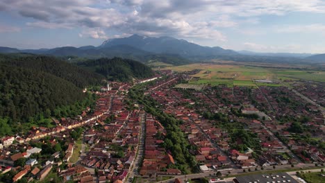 Rasnov-city-with-bucegi-mountains-backdrop,-sunny-day,-aerial-view