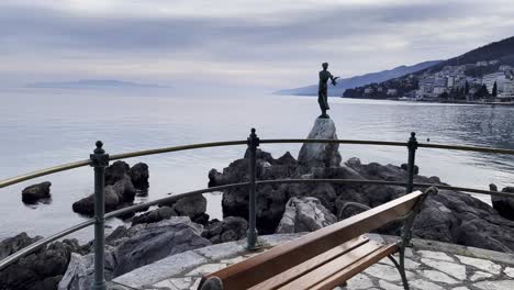 Statue-of-a-woman-on-sea-shore-bench-Resort-town-island-in-distance-Lovran,-Opatija,-Croatia