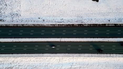 Scenic-aerial-view-of-a-multi-lane-highway,-partially-plowed-and-lined-with-snow-covered-evergreen-trees,-with-a-few-cars-traveling-along-the-road-in-a-winter-wonderland