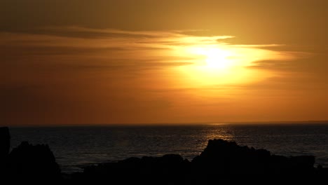 Hora-Dorada-En-El-Mar,-Puesta-De-Sol-Detrás-De-Rocas-Con-Cálidos-Reflejos-Del-Cielo-En-El-Agua,-Tarde-Tranquila