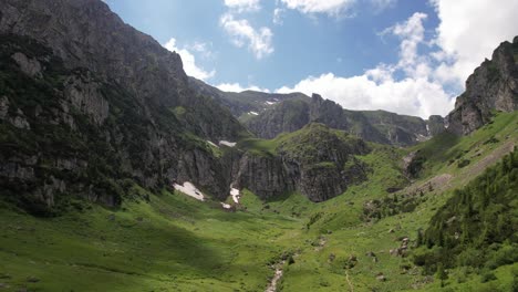 Lush-green-valley-in-Bucegi-Mountains-with-rocky-cliffs-and-waterfall