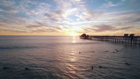 A-tranquil-sunset-seascape-at-Oceanside-California-with-silhouetted-ocean-pier-and-surfers-catching-waves-captured-with-drone-aerial-shot