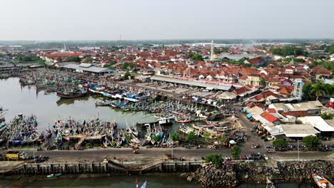 The-hustle-and-bustle-at-the-largest-fish-port-in-Java-is-filled-with-traditional-boats-lining-the-docks,-juxtaposed-to-the-industrial-fishery-area-and-densely-populated-village