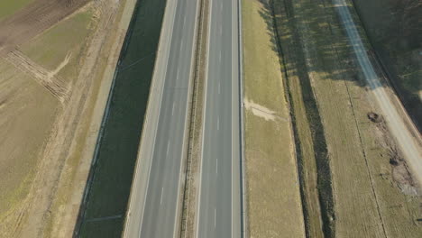 Aerial-view-of-a-highway-with-vehicles-in-motion,-the-road-cuts-through-agricultural-fields-with-distinct-tire-tracks-visible-on-the-sides-of-the-pavement
