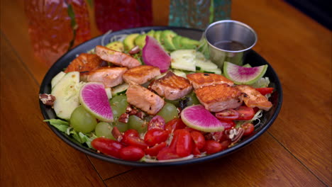 Pull-back-shot-of-a-plate-with-a-healthy-snack-with-grilled-salmon-tomatoes-grapes-cucumbers-radish-and-other-vegetables