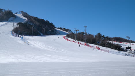 Skiers-on-slopes-of-Alpensia-Ski-Resort,-Pyeongchang,-uphill-panning-view