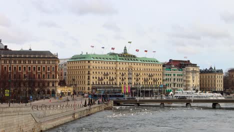 Grand-Hotel-überblickt-Bach,-Während-Busse-Die-Brücke-überqueren,-Auf-Dem-Dach-Wehen-Flaggen