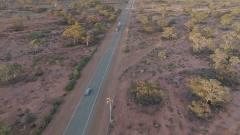 Drone-clipe-showing-road-train-and-vehicles-driving-along-straight-road-through-desert-landscape