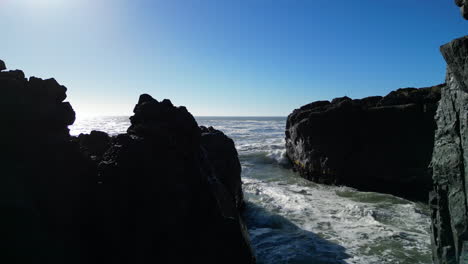 Drone-shot-above-the-ocean,-flying-backwards-into-a-cave