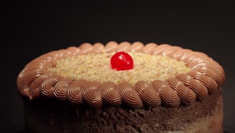 Close-up-detail-shot-Mocha-cake-in-a-turn-table-with-black-background-mocca-moka-mochachino-with-shiny-cherry-on-top-fresh-delicious-tasty-dessert-party-celebration