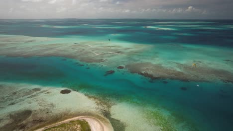Turquoise-waters-and-coral-reefs-with-kite-surfers-gliding,-aerial-view