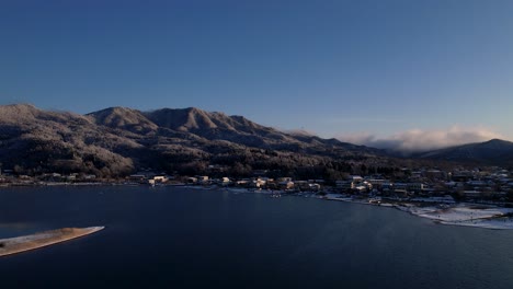 Small-Japanese-Town-Next-To-Lake-With-Snow-Covered-Hills-In-Winter
