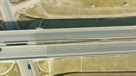 Vista-Aérea-De-Una-Autovía-Con-Un-Solo-Coche-Blanco-Circulando-Por-El-Carril-Derecho,-En-Medio-De-Extensos-Campos-Bajo-Un-Cielo-Despejado.