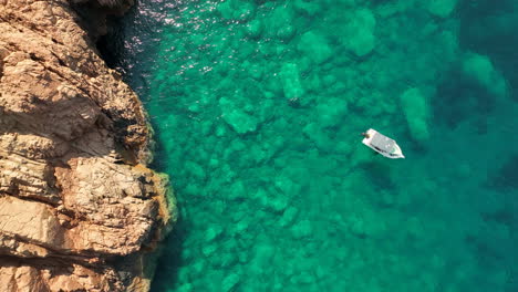 Boat-floating-on-crystal-clear-waters-near-the-rocky-coasts-of-Girolata,-Corsica,-aerial-view