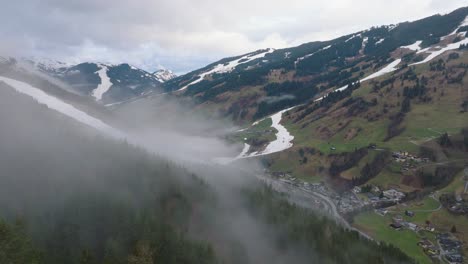 Saalbach-Hinterglemm-with-fog-over-mountains-and-village-at-dusk,-aerial-view