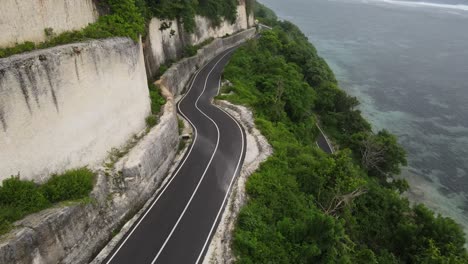 Aerial-view,-cliffside-asphalt-road-and-sea-located-on-Tanah-Barak-beach,-Bali-island,-Indonesia