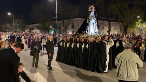 shot-of-the-image-of-the-virgin-with-her-20-bearers-in-clothing-from-the-brotherhood-all-at-a-common-pace-behind-the-ministers-or-priests-everything-takes-place-at-night-there-are-reporters-filming