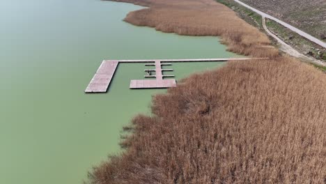 Flying-over-lake-and-fishing-platform-next-to-field-of-grass-in-a-sunny-day-|-Flying-over-field-of-hay-next-to-lake-|-Beautiful-spring-tall-grass