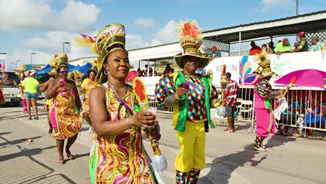 Caribbean-men-and-women-hold-drink-and-staff-in-hand-marching-down-street-during-Carnaval-parade