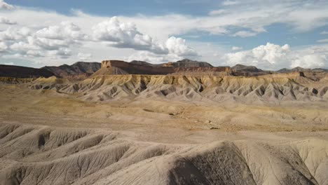 A-spectacular-4K-drone-shot-over-the-barren,-desert-hills-of-Grand-Valley-OHV-area,-with-the-steep-sloped-plateaus-of-the-Little-Book-Cliffs-in-the-distance,-located-in-Grand-Junction,-Colorado