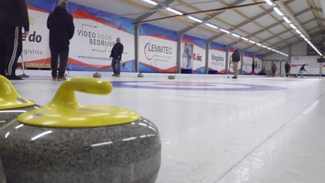 Curlingstein-Aus-Gelbem-Granit-Mit-Leuten-Im-Hintergrund,-Die-Curling-Auf-Dem-Eis-Spielen---Antwerpen,-Belgien