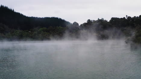 Fly-through-steam-rising-over-volcanic,-geothermal-lake-in-New-Zealand,-North-Island