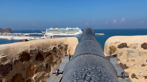 A-canon-over-the-Gulf-of-Oman-at-Muttrah-Fort-with-a-cruise-ship-in-the-port